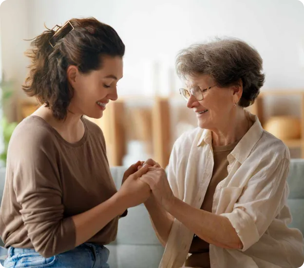 A woman holding an older woman’s hands and smiling